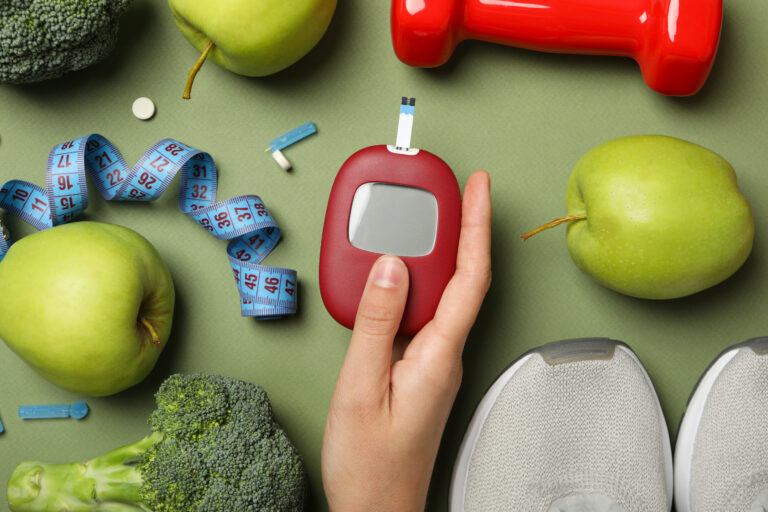 Mão segurando um aparelho de glicemia e fita métrica ao fundo, representando a relação entre controle glicêmico, nutrição e suplementação probiótica em pacientes com diabetes.