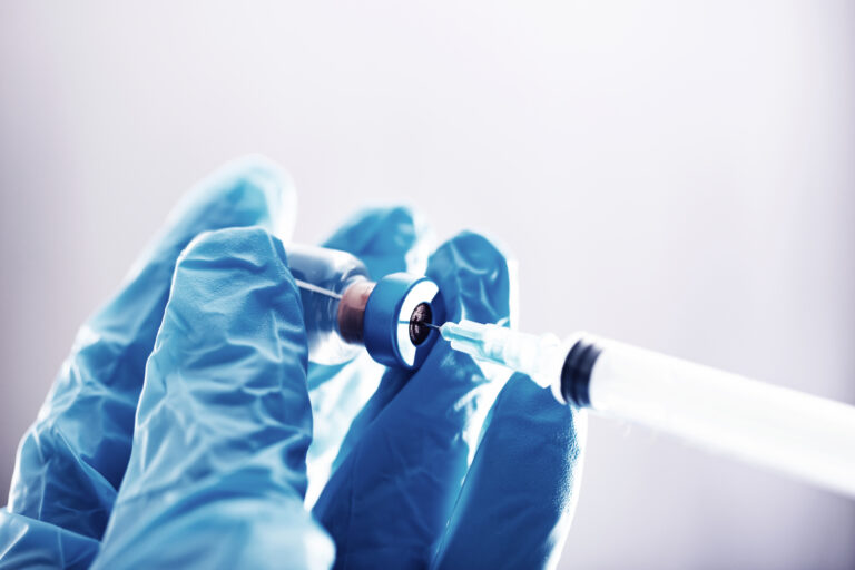 Profissional de saúde com luvas azuis prepara uma seringa com vacina em frasco de vidro, representando avanços científicos em imunoterapia contra o câncer