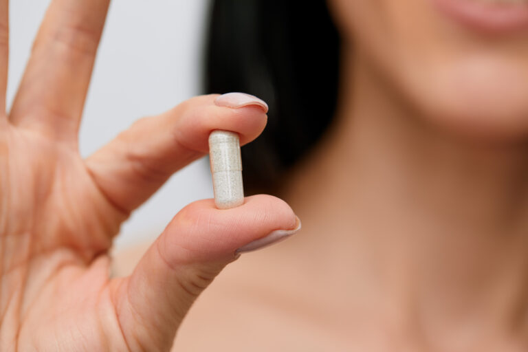 Pessoa segurando uma cápsula de suplemento entre os dedos, em destaque, simbolizando o uso de ingredientes funcionais como beta-glucanas de levedura para suporte à imunidade.