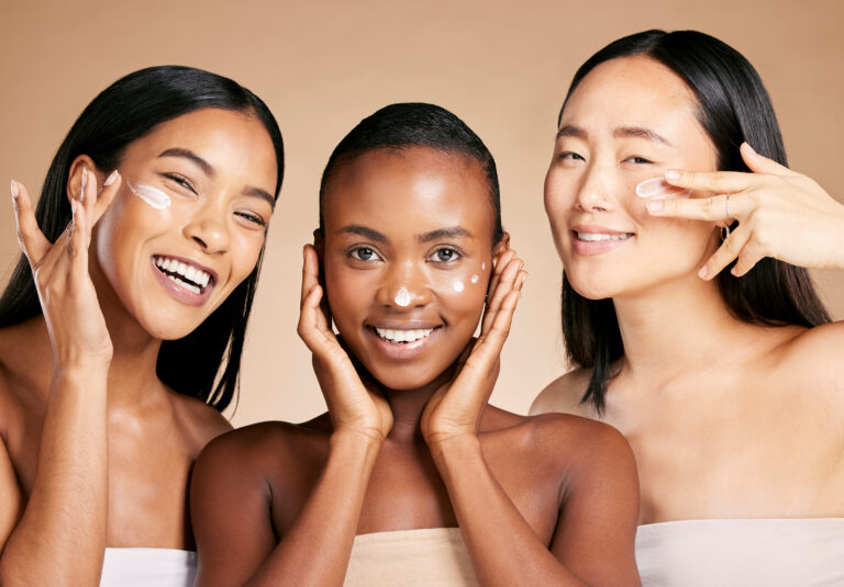 Três mulheres de diferentes tons de pele aplicando creme facial, representando diversidade, cuidado com a pele e rotinas de skincare focadas no equilíbrio do microbioma cutâneo
