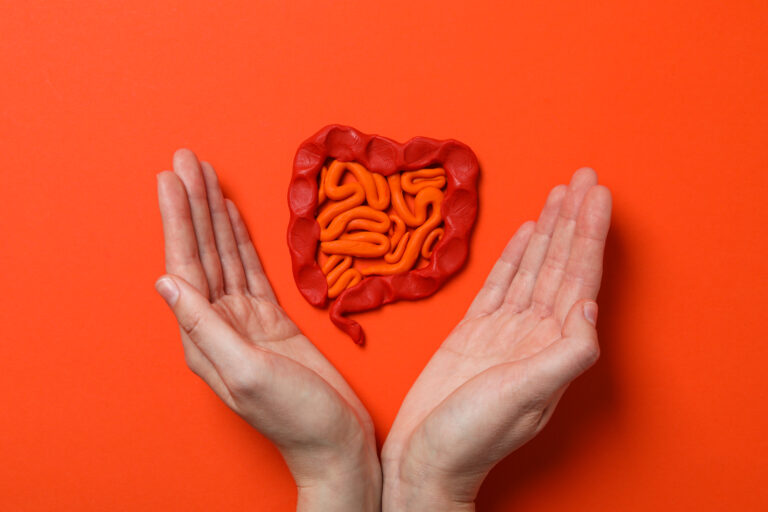 Mãos humanas envolvem uma representação do intestino em fundo laranja, simbolizando o cuidado com a saúde intestinal e o papel do microbioma no bem-estar do corpo.